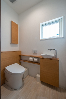 ホワイトのトイレや壁に木材のカウンターでナチュラルな雰囲気のトイレ